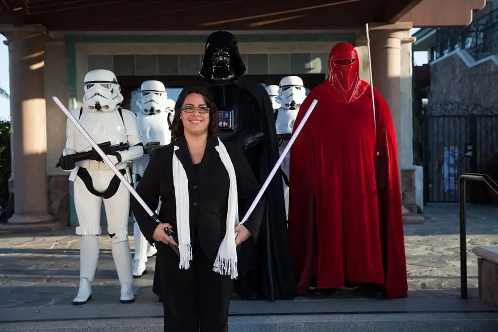Minister Marie of Let's Get Married by Marie proudly carries lightsabers to the newlywed couple with stormtroopers, an Imperial guard, and Darth Vader escorting her