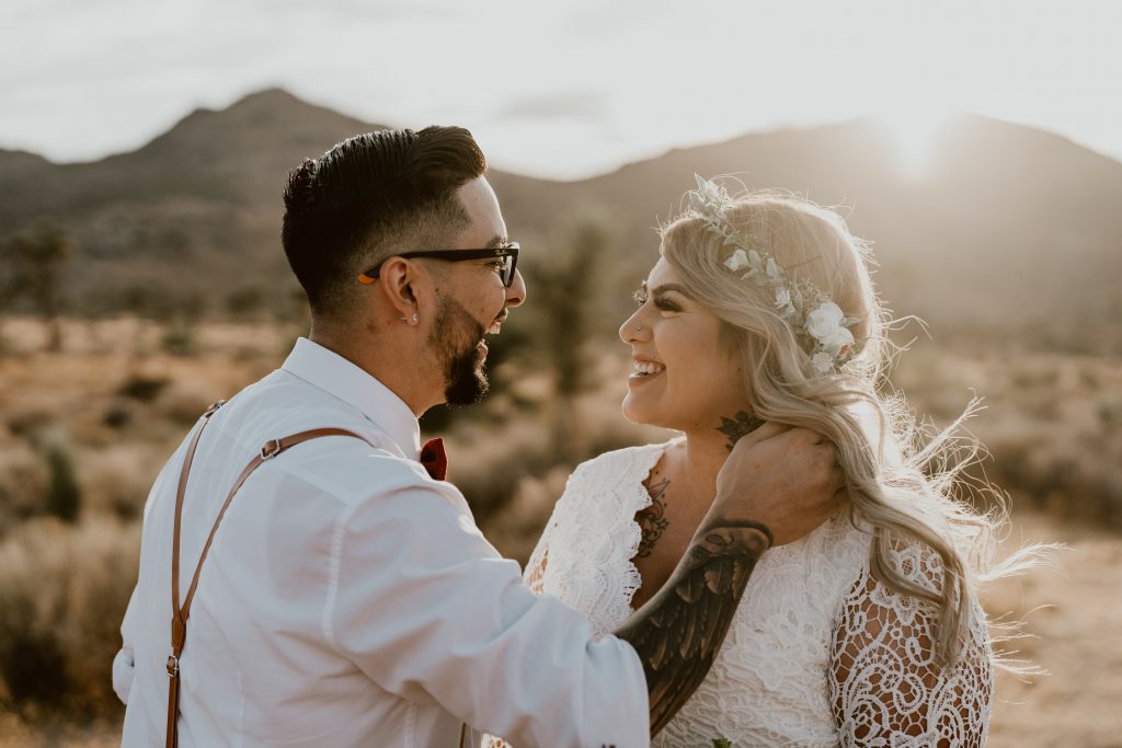 A new husband smiles at his boho bride in a white flower crown while eloping in Joshua Tree with Let's Get Married by Marie
