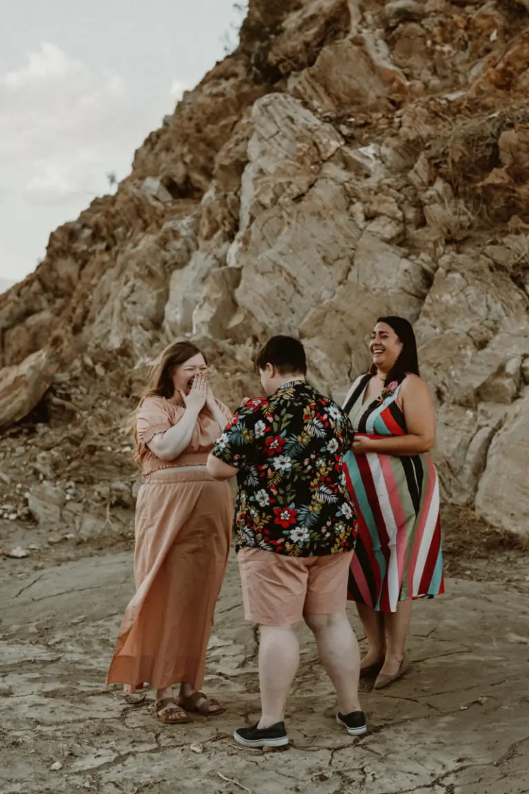 Palm Springs elopement packages with Let's Get Married by Marie features two brides, one in a pink dress who is laughing and wiping away tears, and another in shorts and a print shirt reading her vows