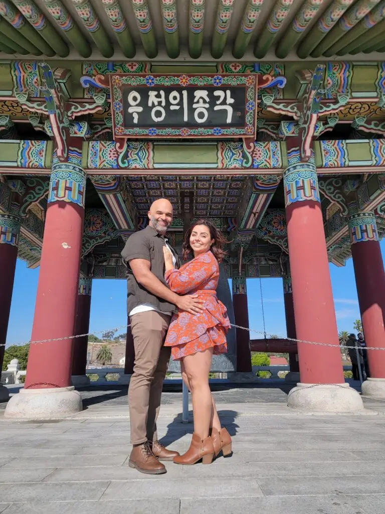 a couple hold each other in front of the Korean Friendship Bell after their vow renewal with Let's Get Married by Marie